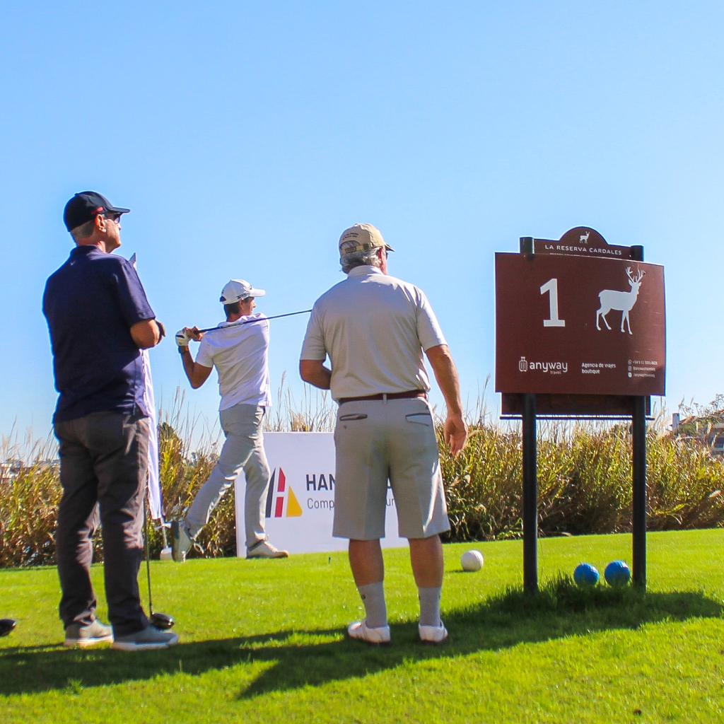 Three people getting ready to tee off at hole 1 in La Reserva Cardales under a clear blue sky.
