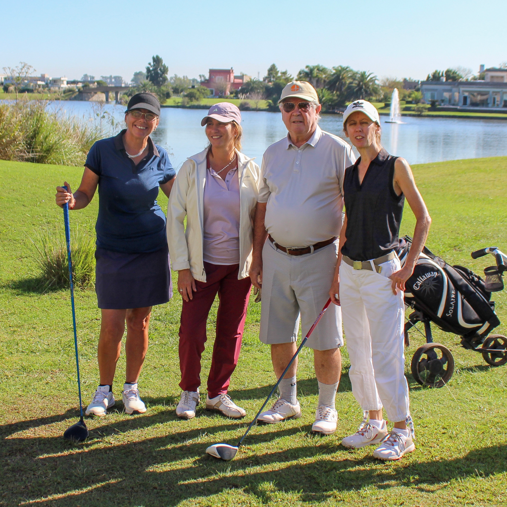 Two women and two men smiling by a lake on the golf course, ready to play.