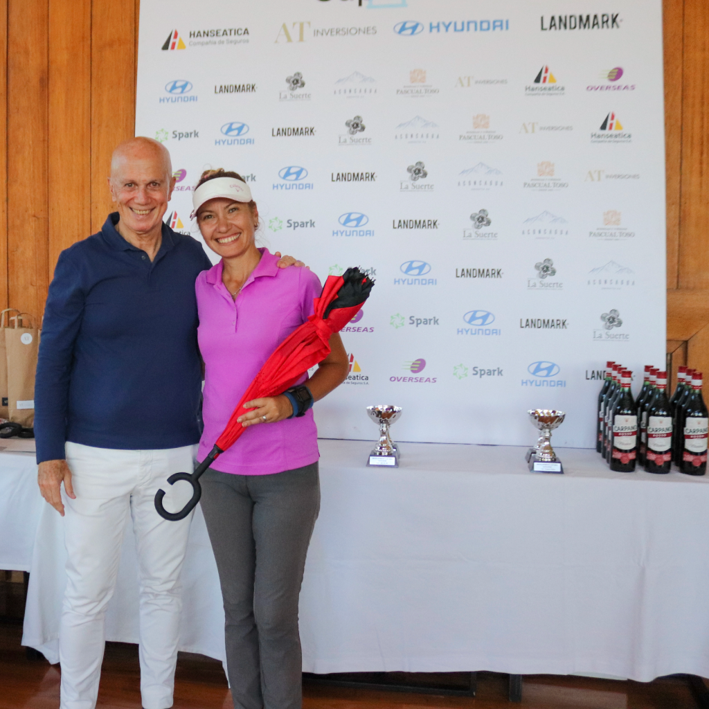 A smiling woman receives a prize and poses with a man in front of the event sponsor backdrop.